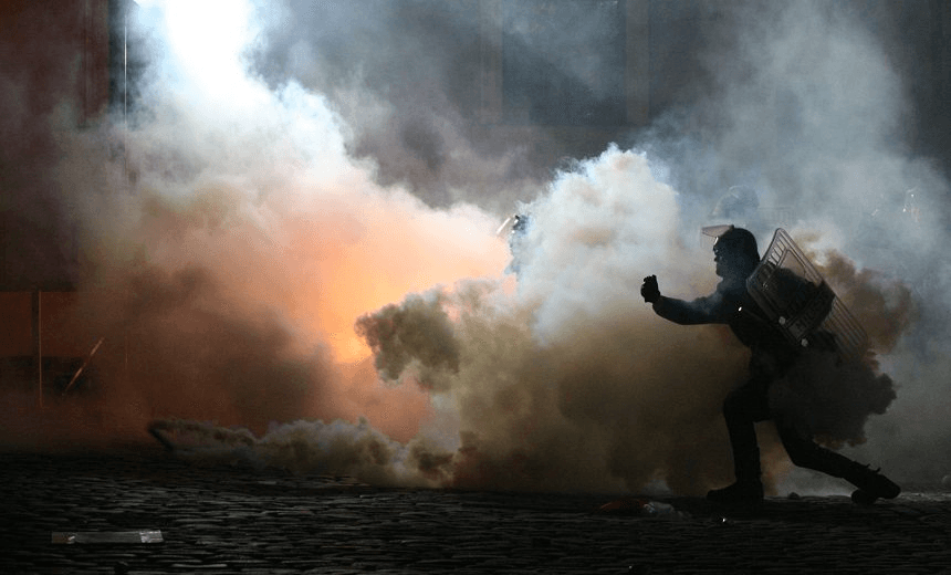 Policjant rzuca gaz dymny w demonstrant?w. 
