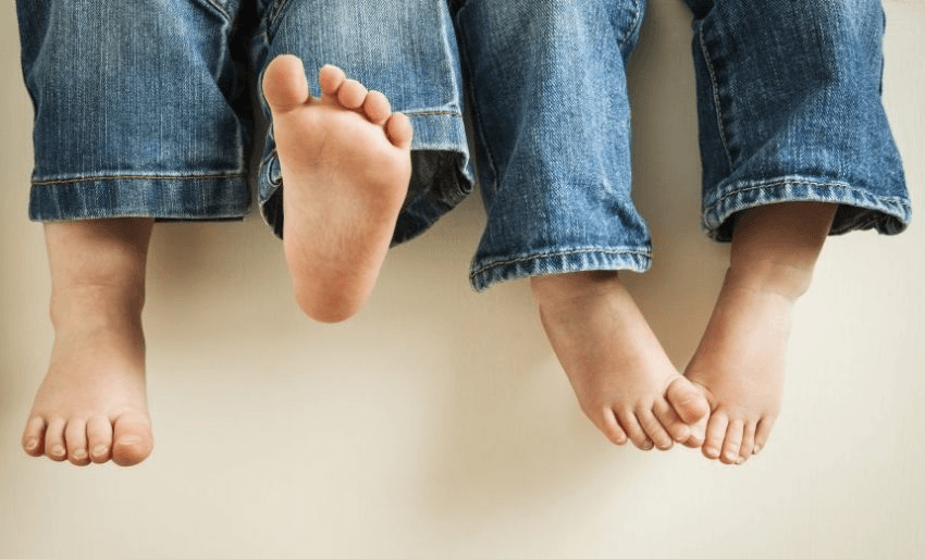 Two children's legs wearing jeans swinging feet.