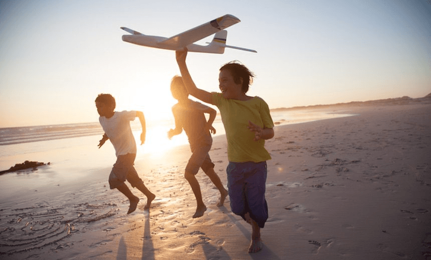 Boys running along beach with a toy plane