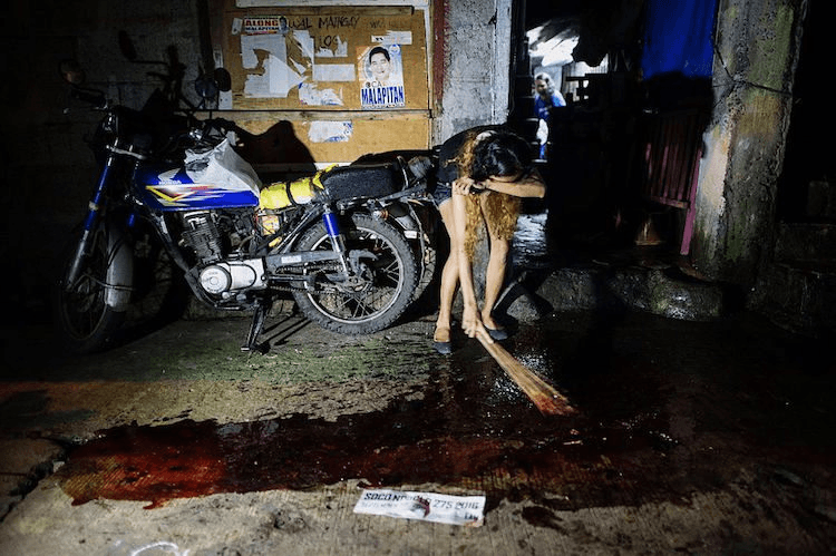 A relative cries as she sweeps the blood of a relative gunned down by unidentified killer in Manila, September 22, 2016. (Photo: NOEL CELIS/AFP/Getty Images)