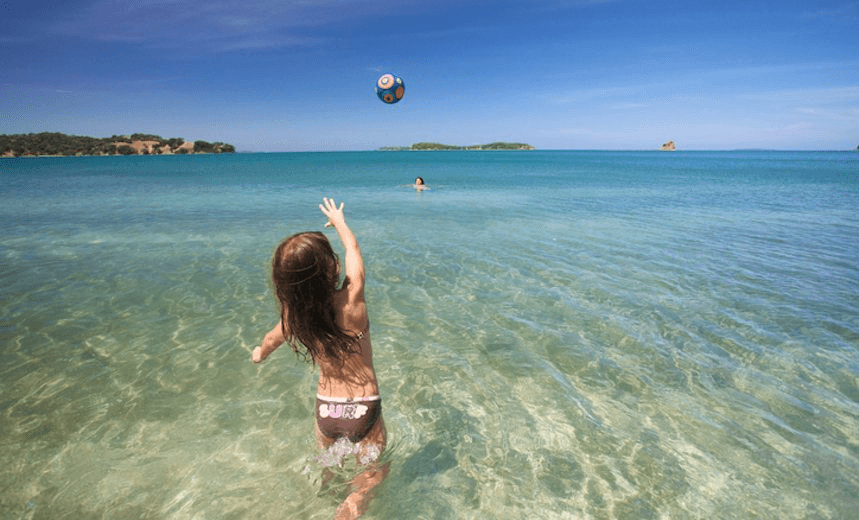 Little girl throwing beach ball in sea at  Sullivans Bay, Mahurangi Regional Park. 
