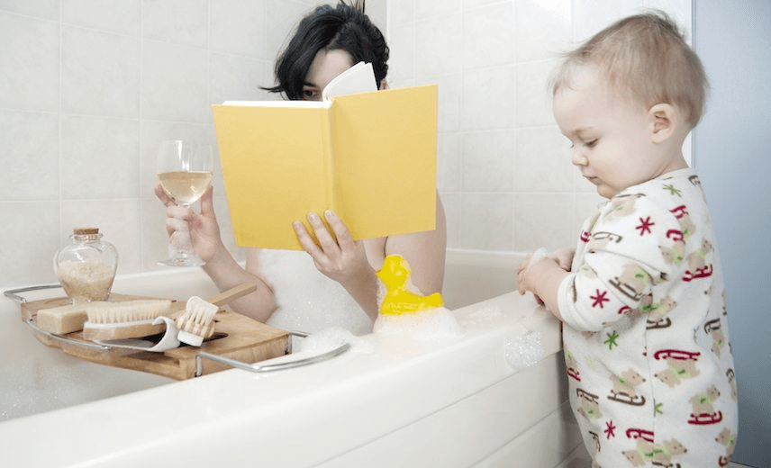 Mother in bathtub with toddler beside tub