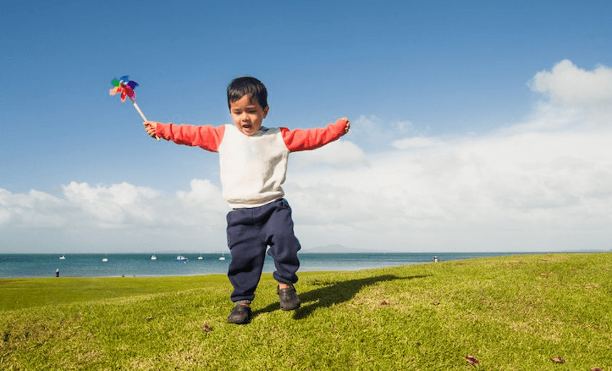 A kid in park playing with paper pinwheel . 
