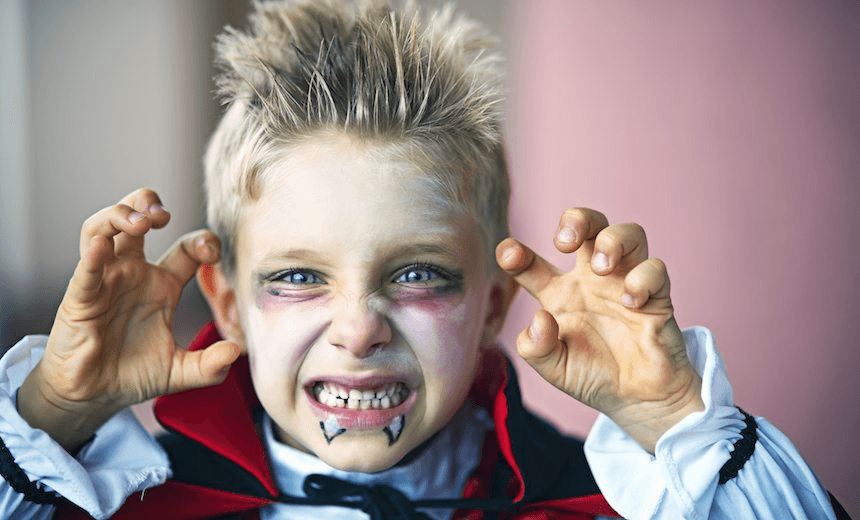 Portrait of a little boy dressed up as halloween vampire. The boy is aged 6 and is making scary face at the camera. 
