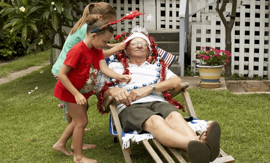 Children decorating senior man with Christmas decorations in yard