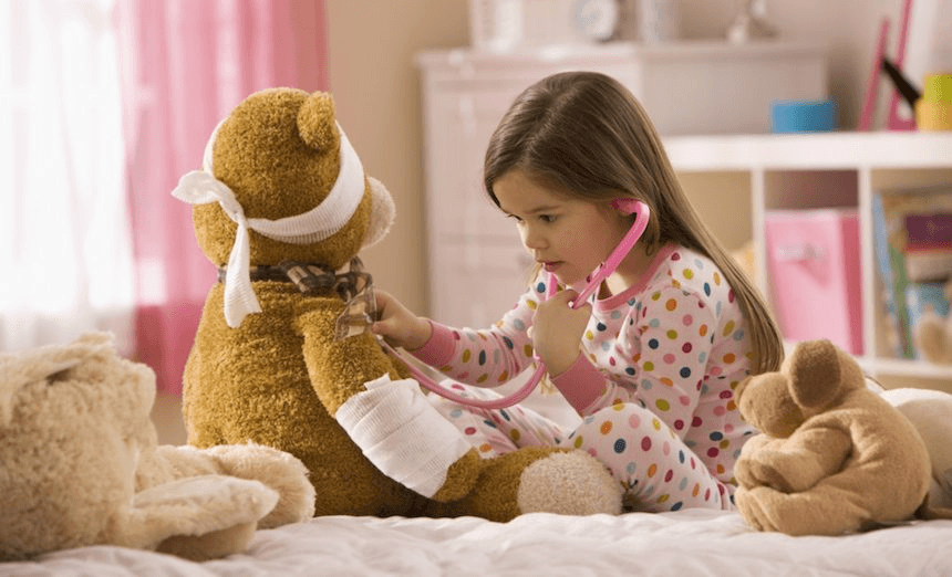 Mixed race girl playing doctor with stuffed animal 
