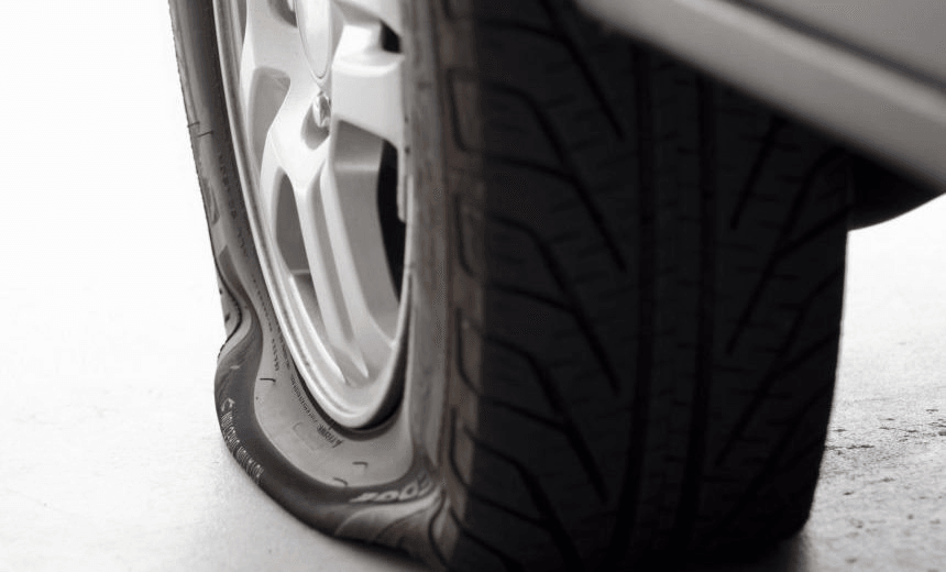 Flat tire on a passenger vehicle sitting on a garage floor, left side of image fades to white. 
