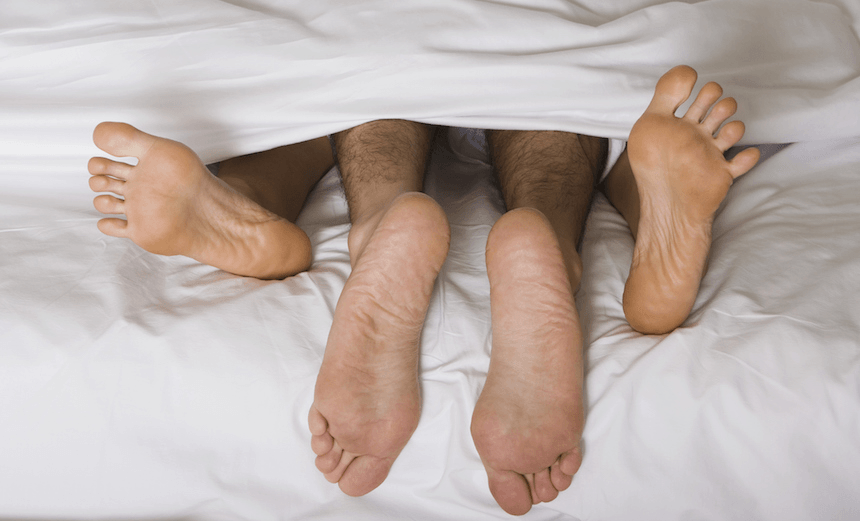 High angle view of a couple&#8217;s feet under the sheets of a bed