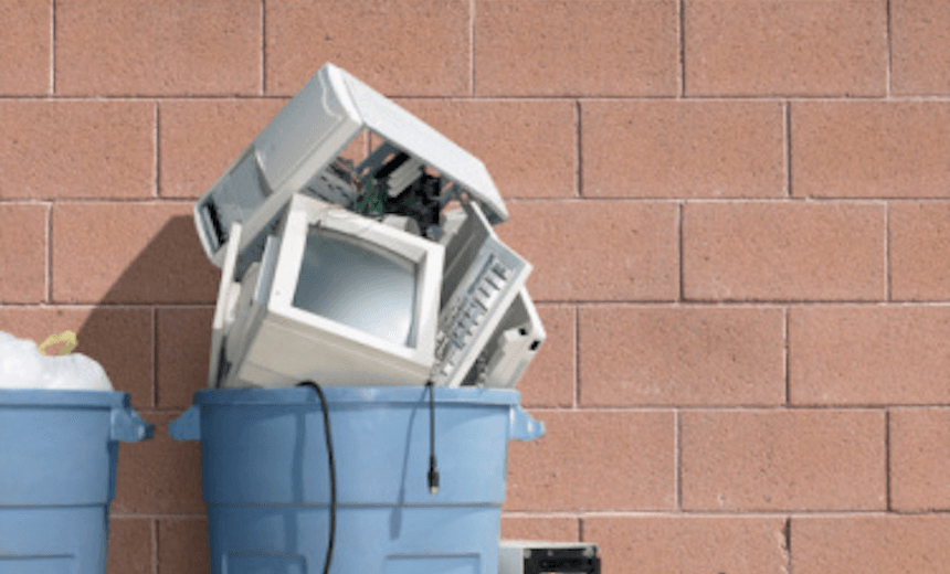 Trash can filled with computer tower, monitor and keyboard 
