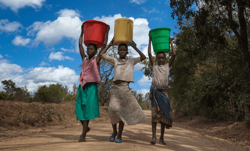 Teenage girls carry water from a borehole, in southern Malawi. Three teenage girls carrying colorful buckets of water on a dirt road, returning from their journey to the nearest borehole, in Balaka District, southern Malawi, under a blue sky with clouds. 
Photo: Guido Dingemans, De Eindredactie / Getty 
