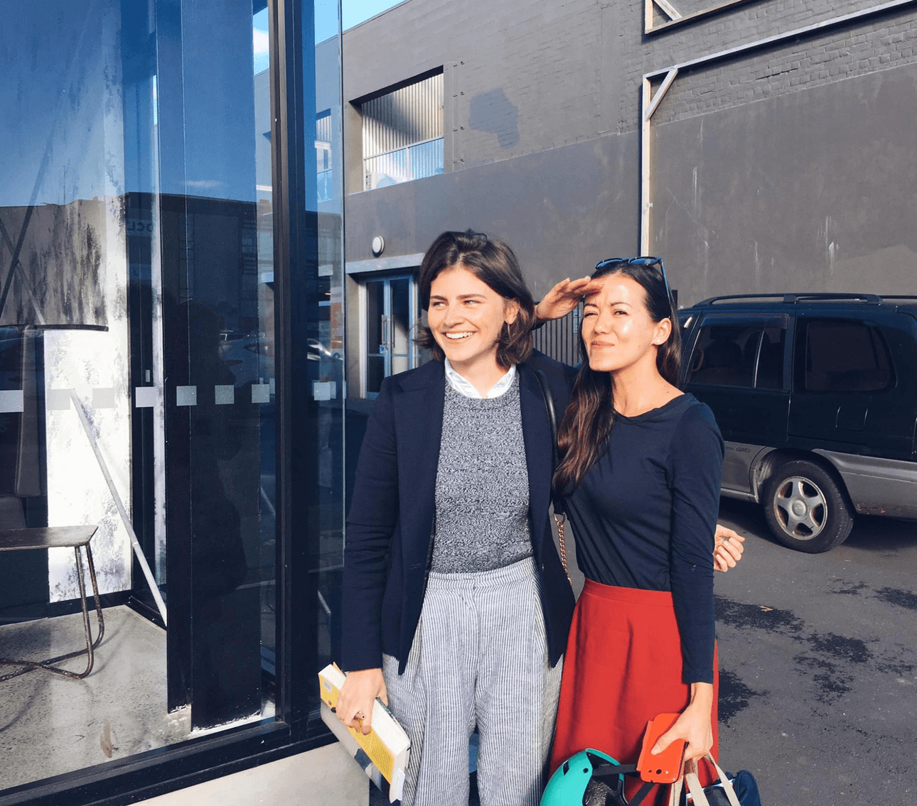 two women standing together in the sunshine, one is light skinned with brown hair and one is brown skinned and petite with black hair