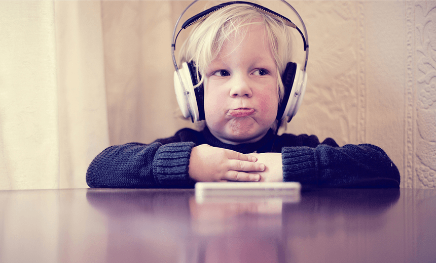 Little boy listening story on his headphones and smart phone with sad face. 
