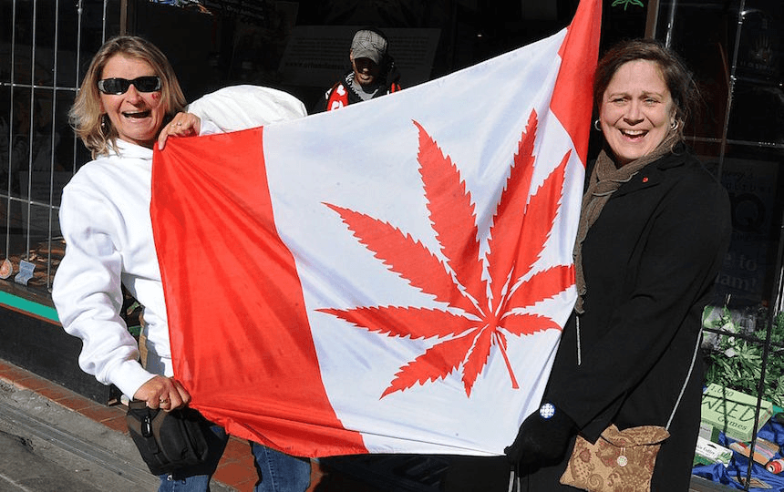 Visitors pose in front of a flag similiar to the Canadian one but showing a cannabis plant instead of a maple leaf at a store in Eastside Vancouver during the Vancouver Winter Olympics on February 22, 2010.         AFP PHOTO/Mark RALSTON      (Photo credit should read MARK RALSTON/AFP/Getty Images) 
