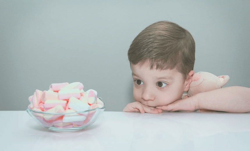 Cute boy hugging his stuffed toy and looking a bowl of marshmallows in white table, in soft pastel colors 
