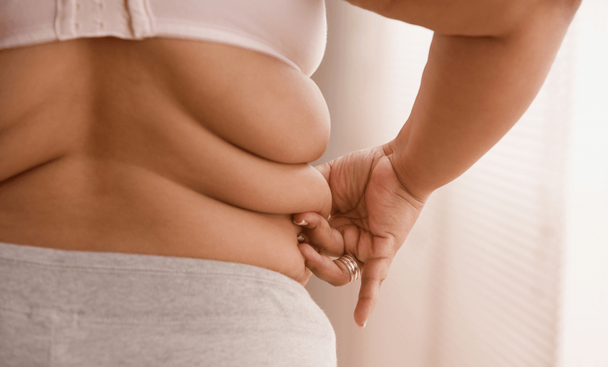 Overweight woman pinching a roll of fat on her side 
