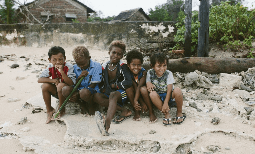 Children of Fanalei sit on what remains of their village church, gradually swept out to see a few years ago (Photo: Jo Currie) 
