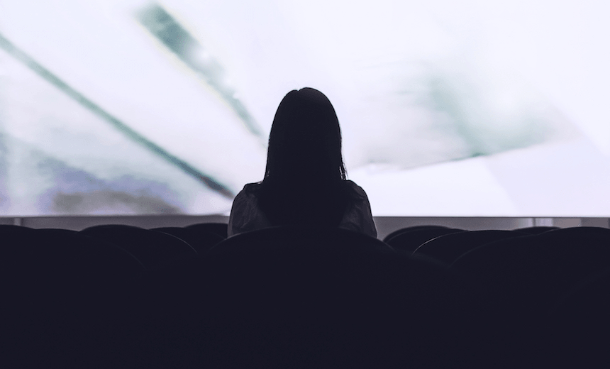 Rear view of woman sitting alone watching movie in empty theatre 
