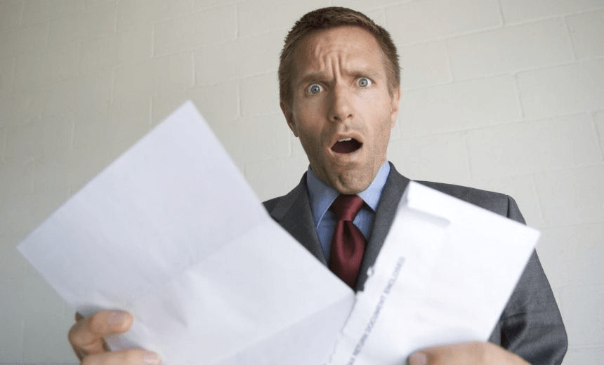 Young man businessman looking up from opening his mail with an expression of outrage 
