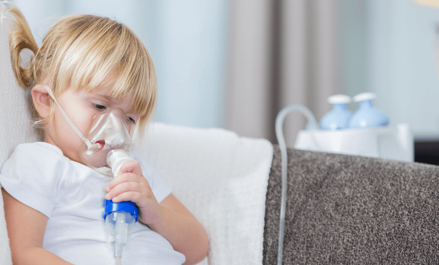 Girl holds an oxygen mask while receiving a breathing treatment. She is sitting on the sofa in her home. 
