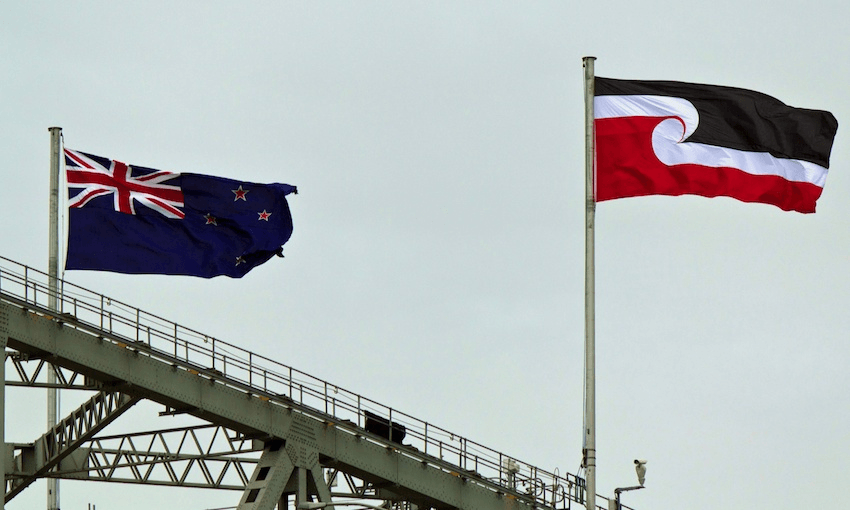The Tino Rangatiratanga flag flies alongside the New Zealand national flag on the Auckland Harbour Bridge during Waitangi Day celebrations (photo: Hannah Peters/Getty Images). 
