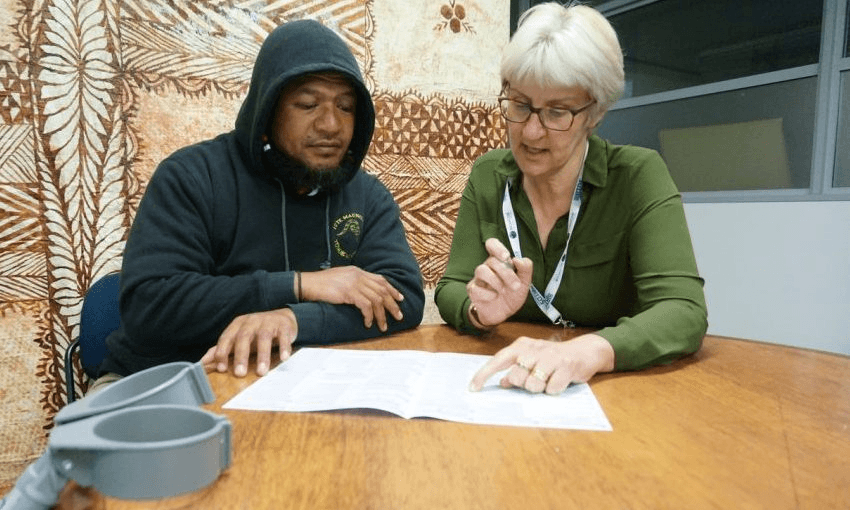 elederly whit woman and brown man in a hoodie look at a sheet of paper with a tapa cloth pattern in the bacground