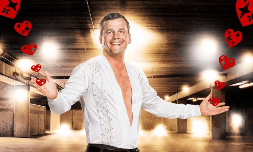 bright lights in the background, a man with lots of fake tan holds his arms wide while wearing a white shirt with a deep v cut to his bellybutton, and a slightly unsettling look in his eyes