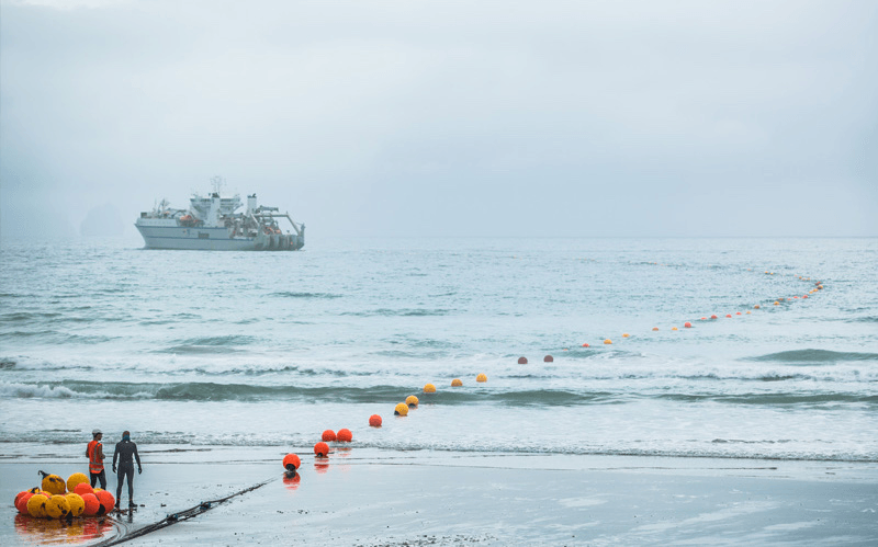 an ocean with some bobbing buoys and a boat and a line whic his the undersea cable 