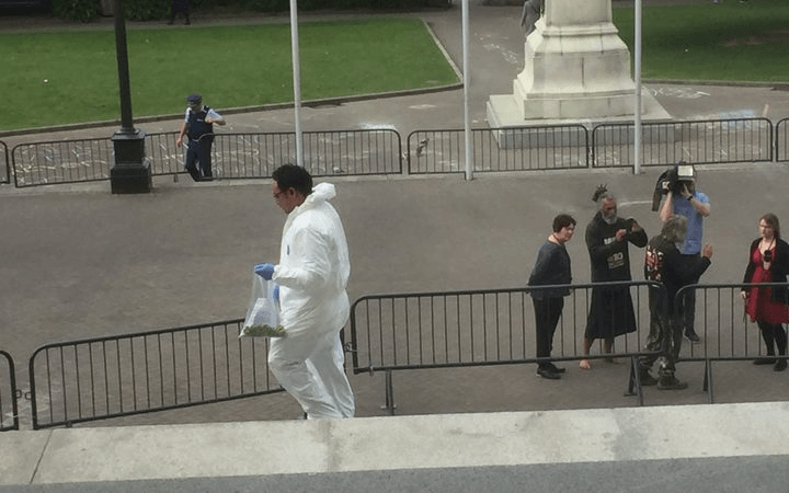 Fake 1080 is cleaned up at Parliament, while an activist is interviewed in the background (Radio NZ: Gia Garrick)  
