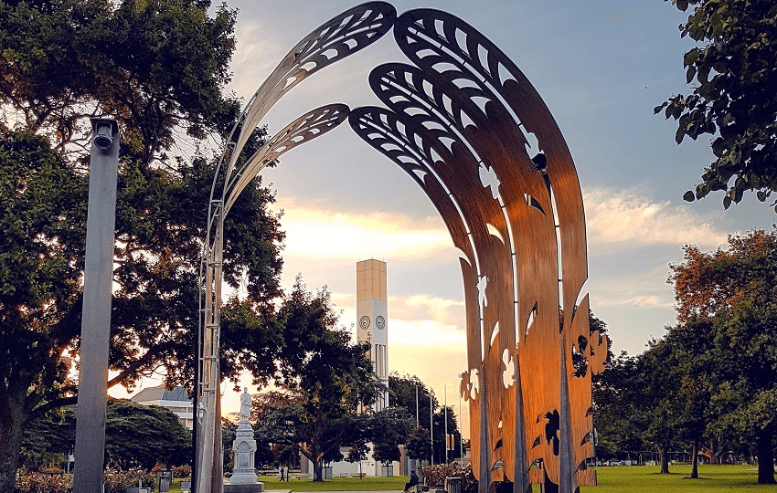 a big arch with feathery bits and trees and some short buildings behind it. good vibes, but this is no metropolis