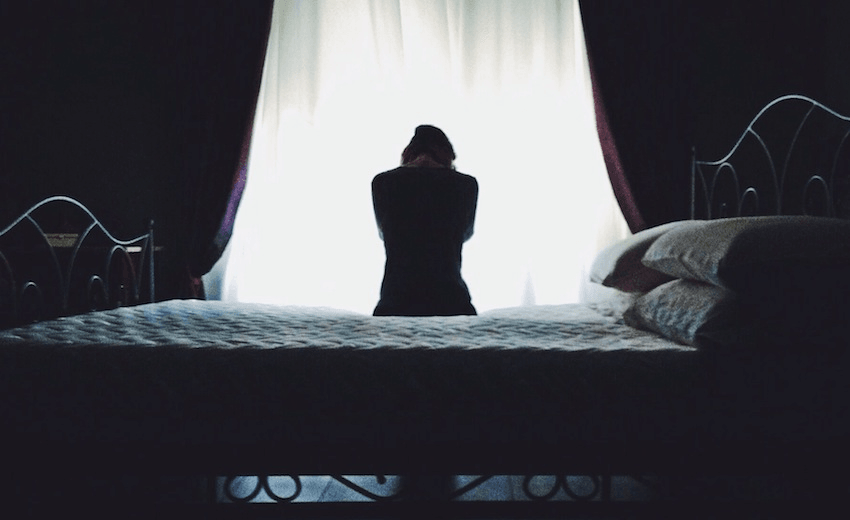 Rear View Of Woman Sitting On Bed Against Curtain