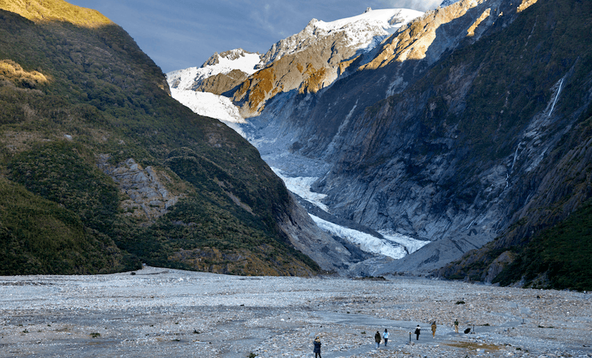 big big mountains with blue sky and a small river of ice between cliffs with people in the foreground