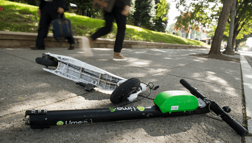 a lime scooter on a footpath with some people in the background. it's in pieces