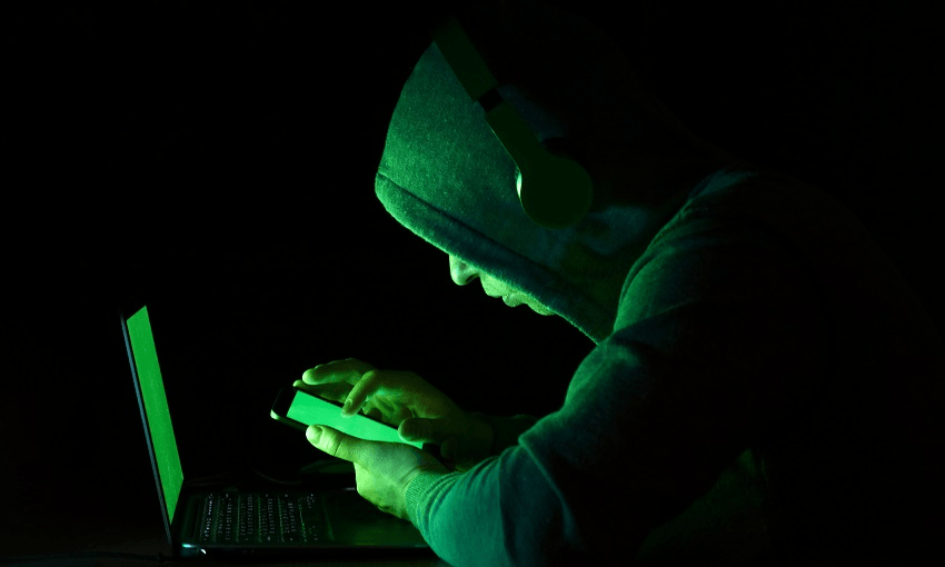 Computer Hacker Using Mobile Phone And Laptop Against Black Background