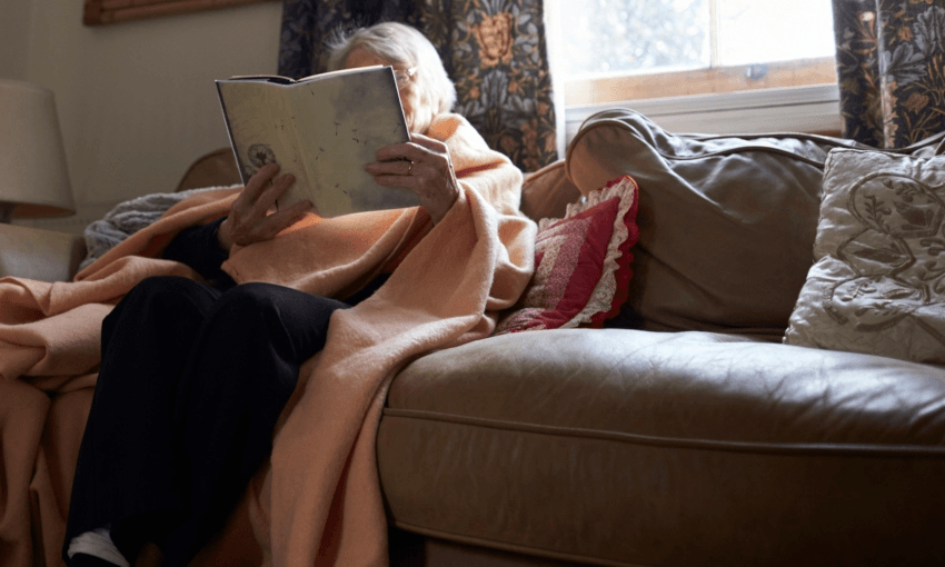 An elderly woman reading under a blanket (Getty Images)  
