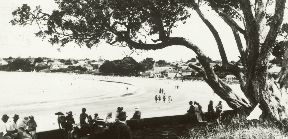 Beachgoers shelter under a pohutukawa, northern end of Takapuna Beach. Auckland Libraries Heritage Collections T0248 
