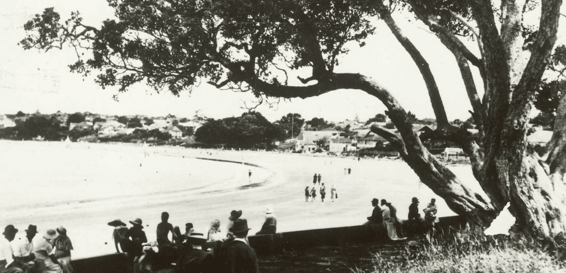 Beachgoers shelter under a pohutukawa, northern end of Takapuna Beach. Auckland Libraries Heritage Collections T0248