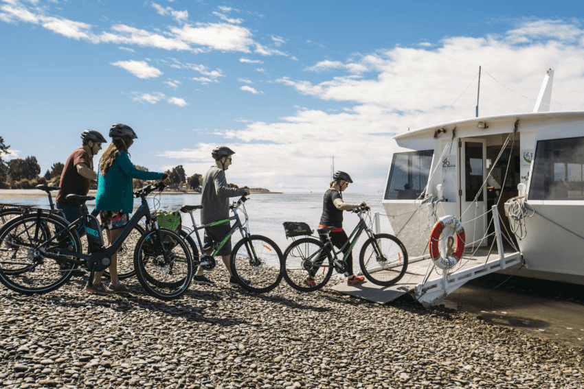 A group of people with bikes, boarding a ferry on Mapua Beach, Nelson region