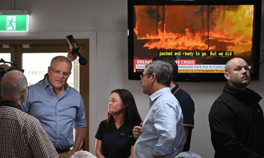 Australian PM Scott Morrison at a NSW evacuation centre, while further fire developments are announced on the TV behind him. (Getty Images)