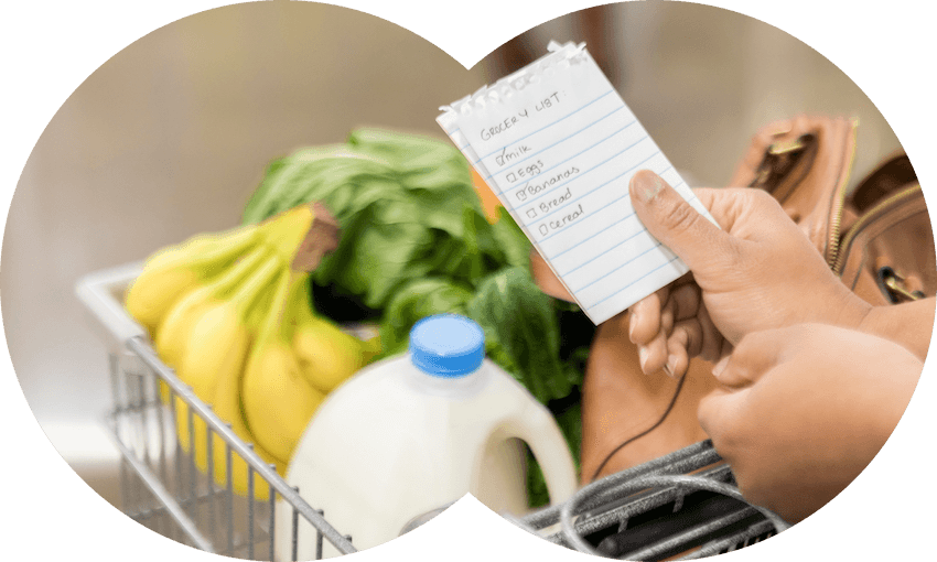 a hand holding a shopping list above a shopping trolley that contains milk bananas and spinach