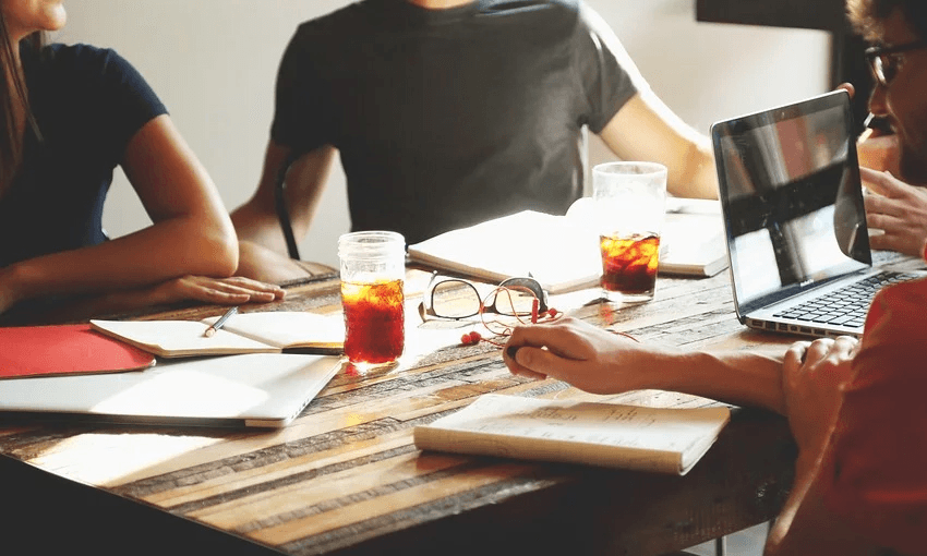 a sunlit desk with hands taking notes and a sense of collaboration in the air
