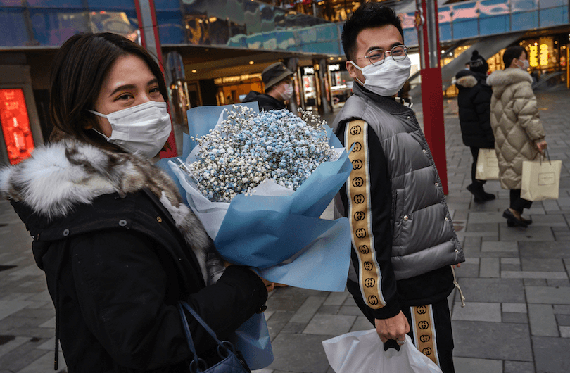 A woman wears a protective mask as she holds flowers given to her on Valentine’s Day at a popular shopping area in Beijing (Photo: Kevin Frayer/Getty Images) 
