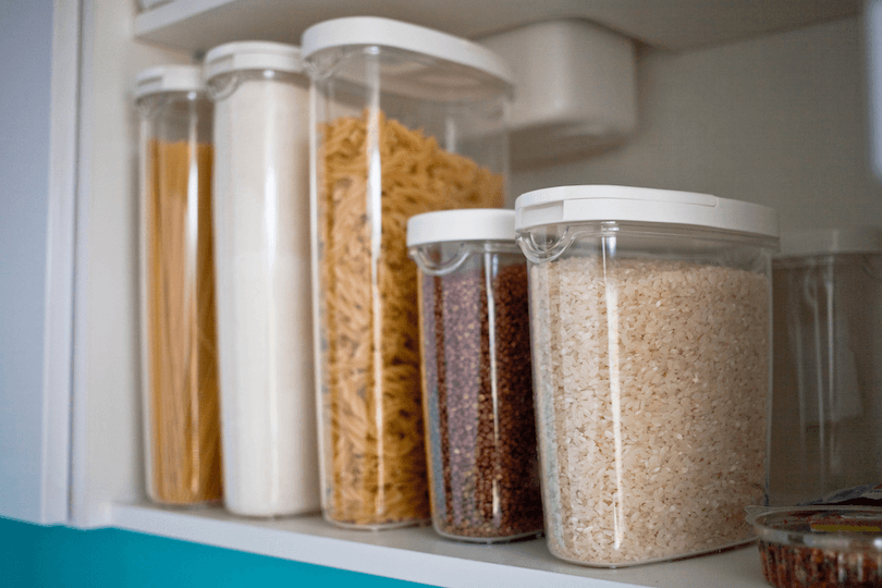 a picture of a pantry with clear plastic containers holding rice, pasta, and sugar