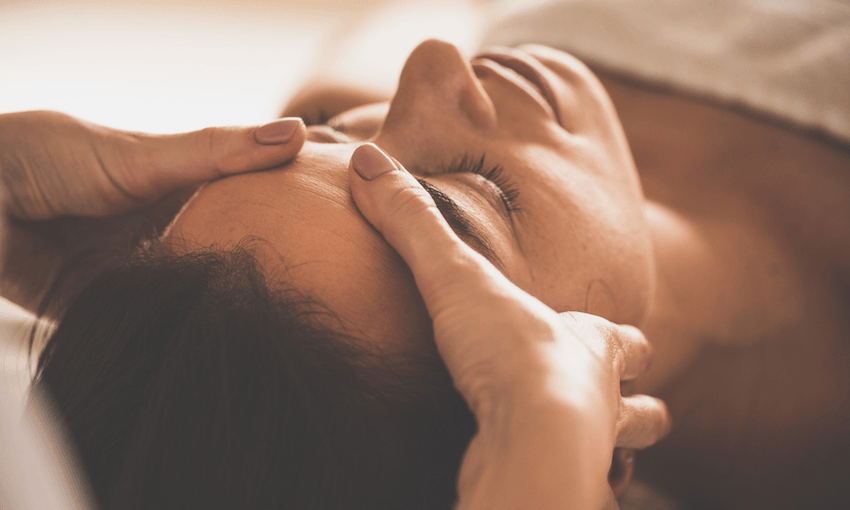 Close-up shot of a massage therapist doing facial massage to her female client at spa. 
