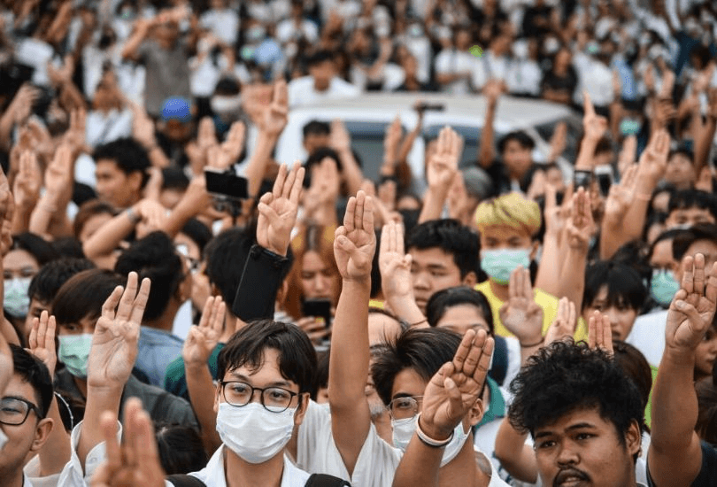 A crowd of university students raising one arm high, with two fingers saluting.