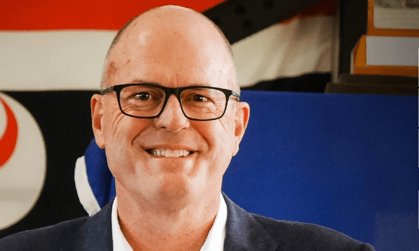 Todd Muller stands in front of flags, one of which was famously hung upside down. 
