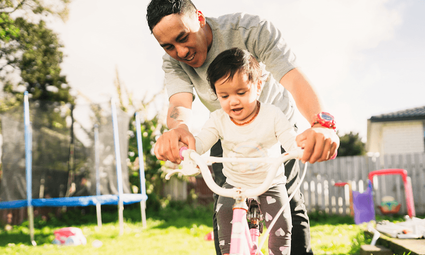Maori father helping his daughter to ride bicycle in backyard.