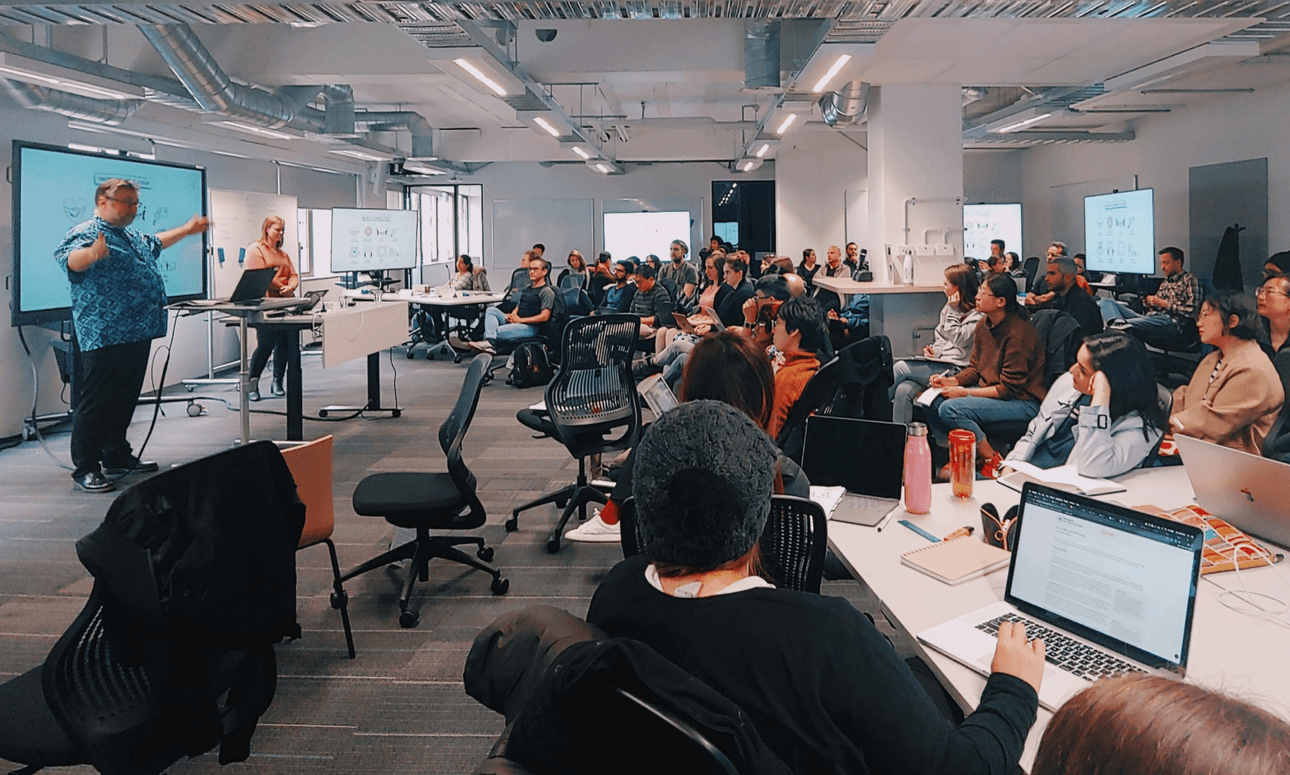 A lecturer stands at the front of a room, educating a group on students on computing concepts.