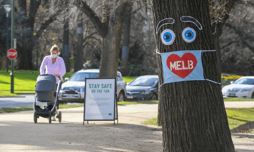 A woman pushes a pram past a large face mask pinned to a tree in Melbourne on August 3  (Photo: WILLIAM WEST/AFP via Getty Images) 
