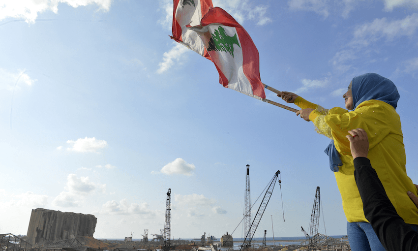 A woman waves a Lebanese flag against the backdrop of the now-destroyed port of Beirut. (Photo: Houssam Shbaro/Getty Images) 
