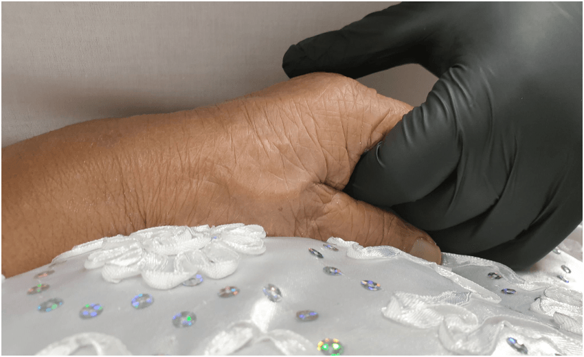 Apulu Reece Autagavaia’s gloved hand holding his grandmother’s hand following her passing (Photo: Supplied)